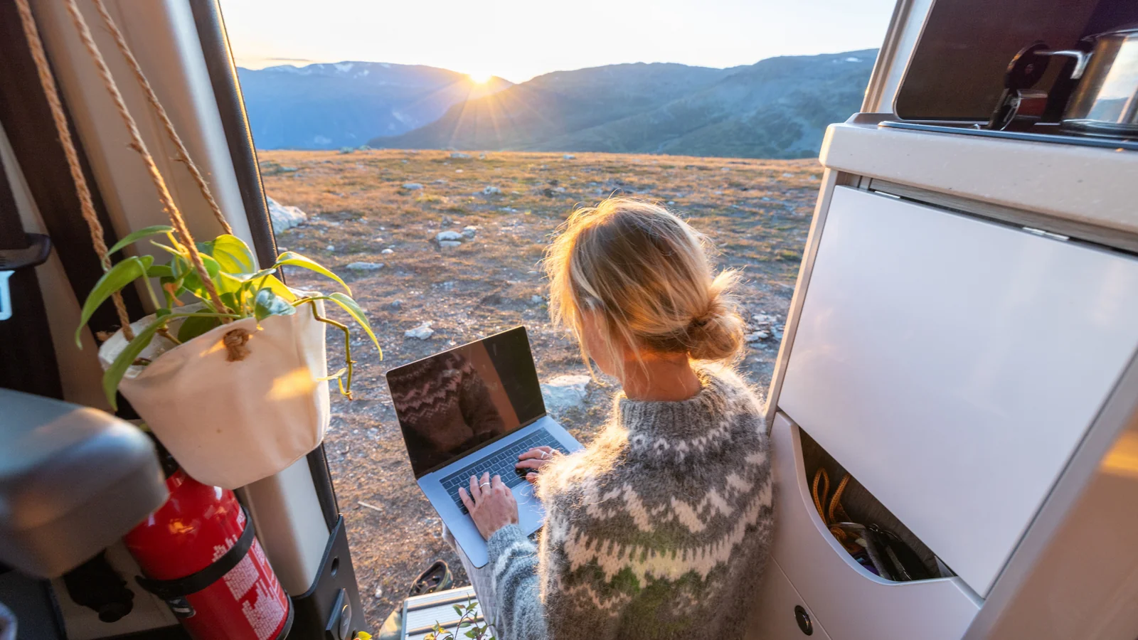 Remote worker with laptop in a campervan at mountain sunset