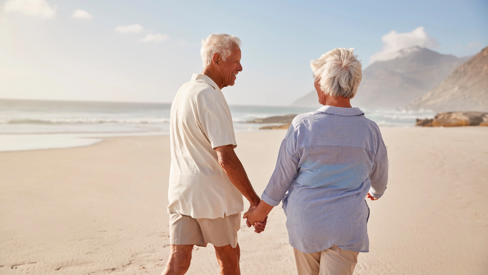 Retired couple walking on the beach with mountains in the background